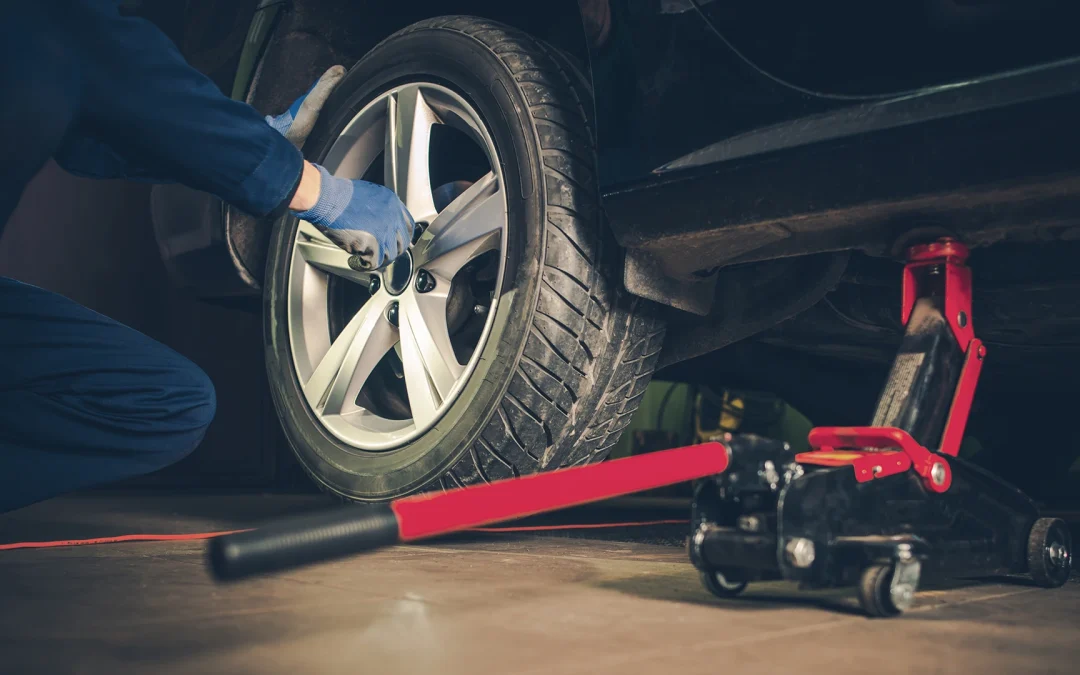 Mechanic replacing a car tire using a jack in an automotive service setting, highlighting tire maintenance relevant to Lethbridge's unpredictable weather.