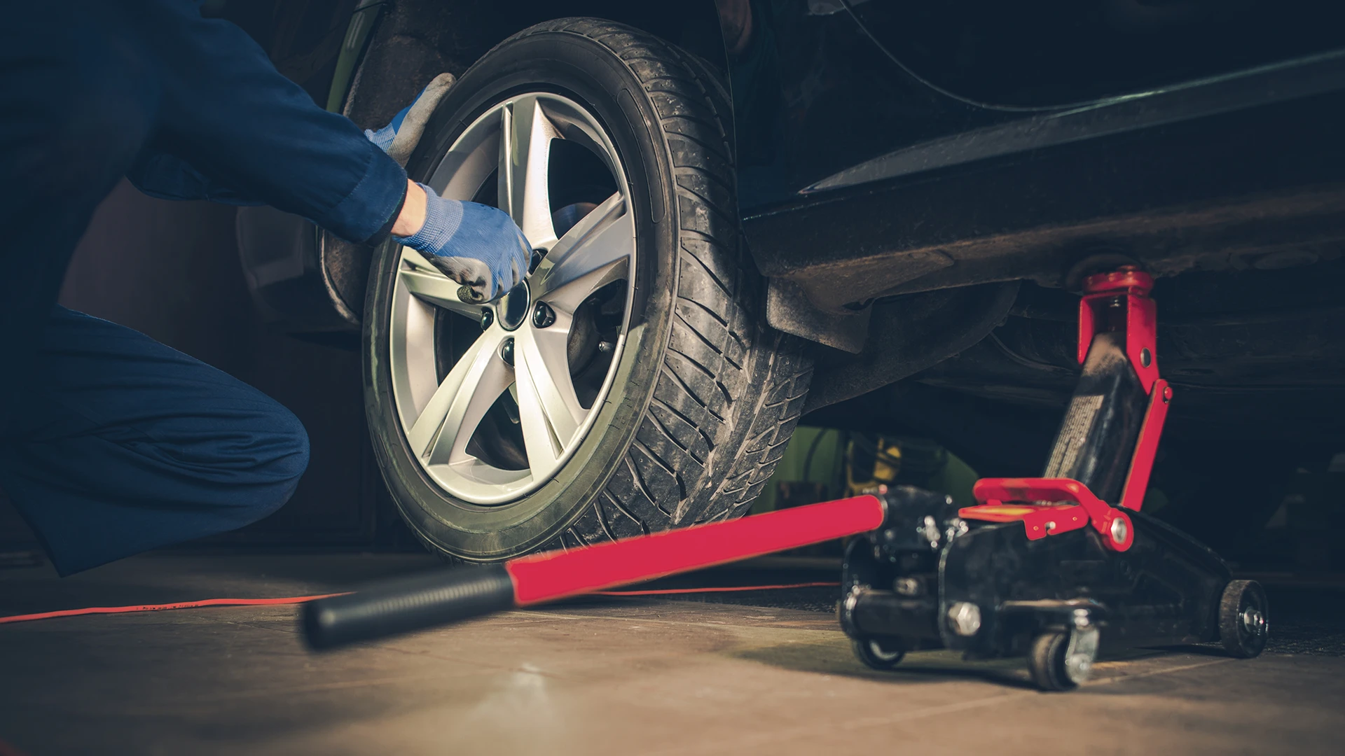 Mechanic using a wrench to change a tire on a car, with a hydraulic jack visible, emphasizing tire replacement services in Lethbridge.